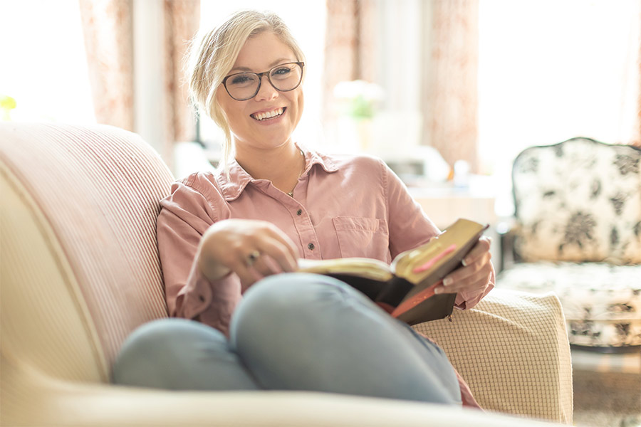 Maggie DeJong sits on the couch smiling and reading her Bible