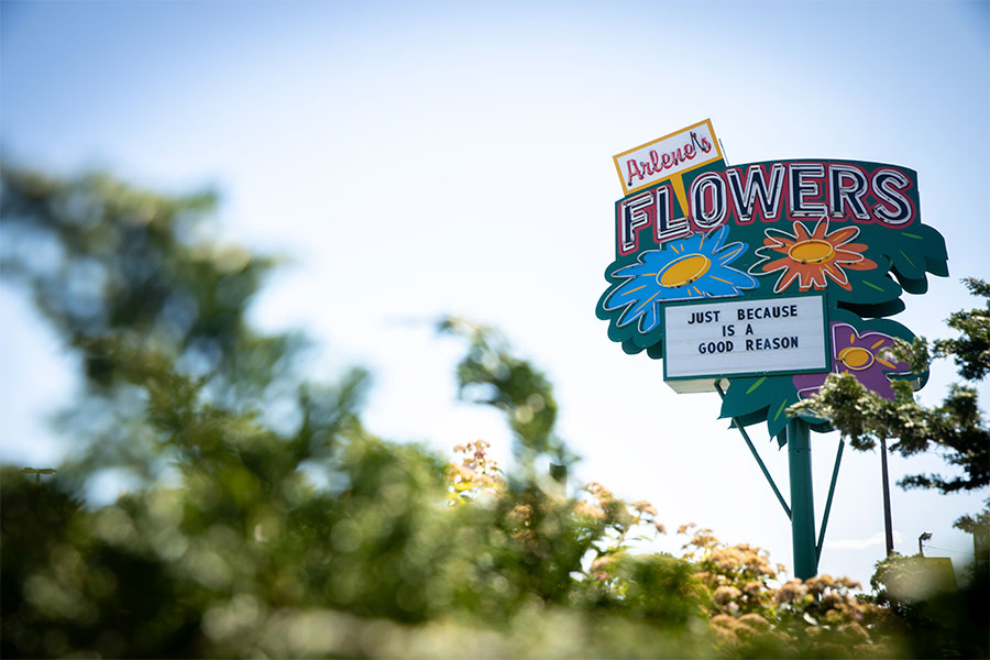 A sign for Arlene's Flowers is seen against a blue sky background on a sunny day.
